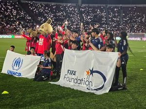 Decenas de niñas y niños reunidos al centro de una cancha de fútbol posan pasa la foto con uniformes deportivos