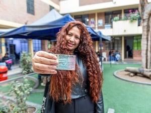 Una mujer de cabello largo rizado sostiene en primer plano con su mano derecha un carné de la República del Perú