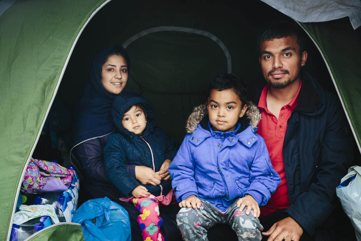Familia solicitante de asilo en Grecia Una pequeña familia de solicitantes de asilo sonríe a la cámara desde el interior de su tienda de campaña en un asentamiento en Grecia.
