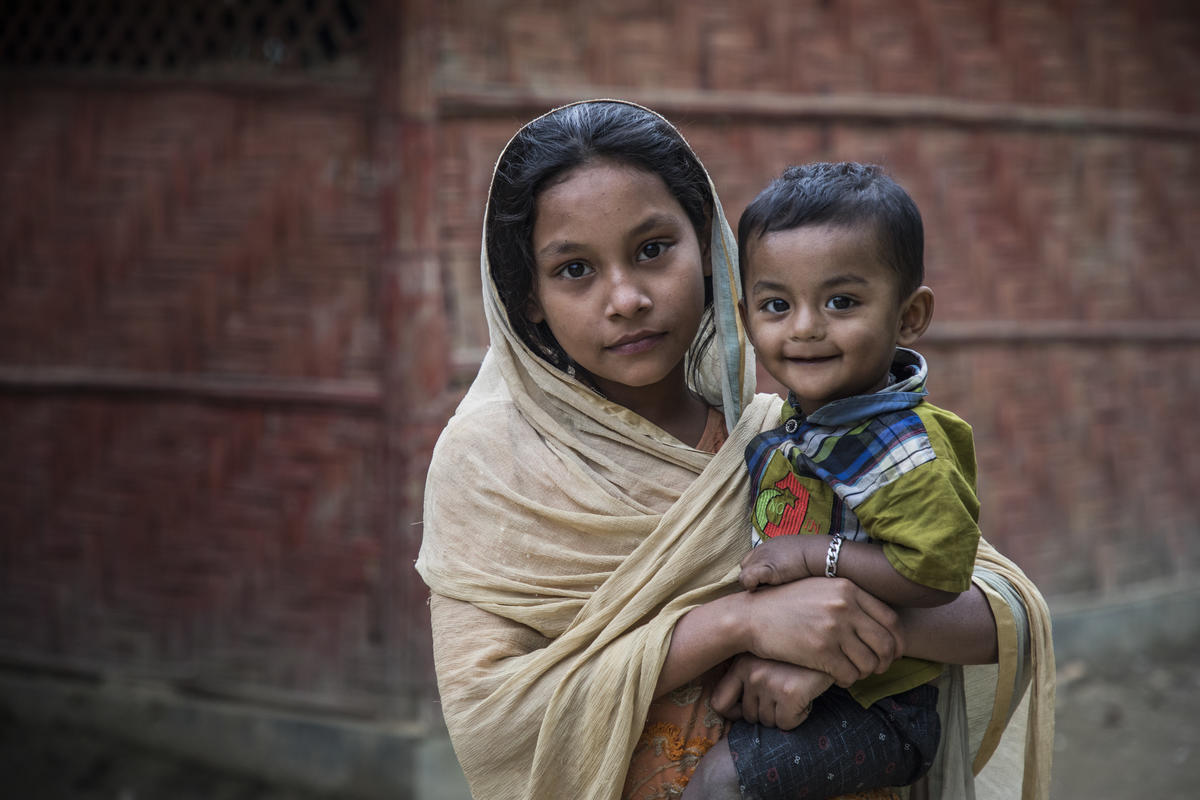 A young Rohingya girl holds her little brother