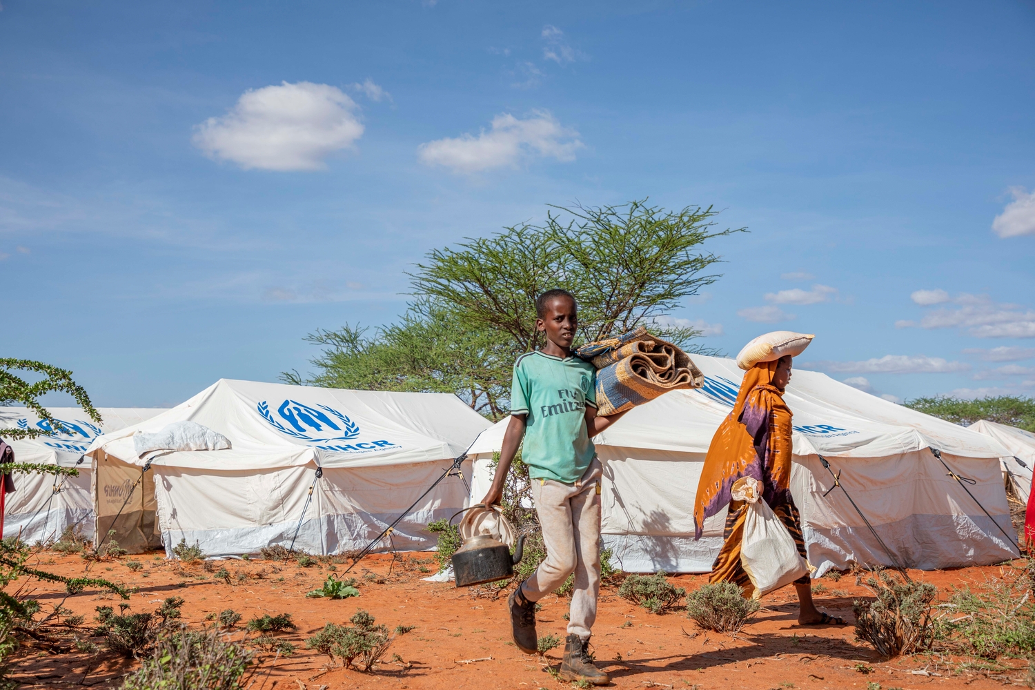 Dos de los hijos de Hinda, Mohamed (izquierda), de 13 años, y Sabarin (derecha), de 16 años, llevan sus pertenencias al alojamiento tras haber llegado al asentamiento de Mirqaan.