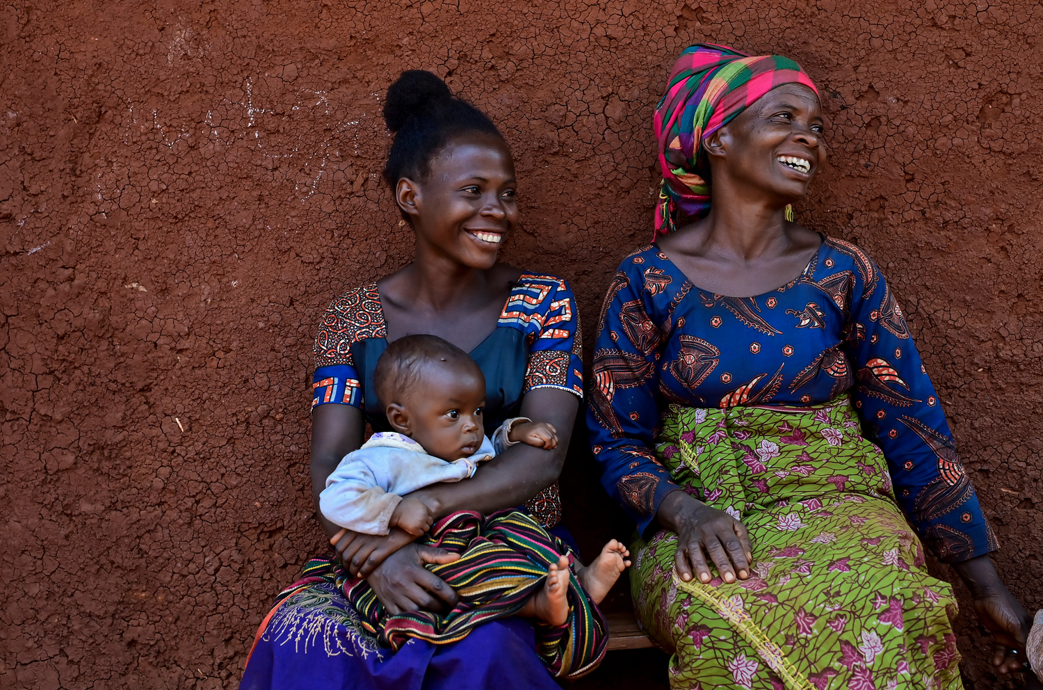 Dos mujeres sonrientes sentadas en una banca, una de ellas con un bebé en brazos. Dos mujeres sonrientes sentadas en una banca, una de ellas con un bebé en brazos.