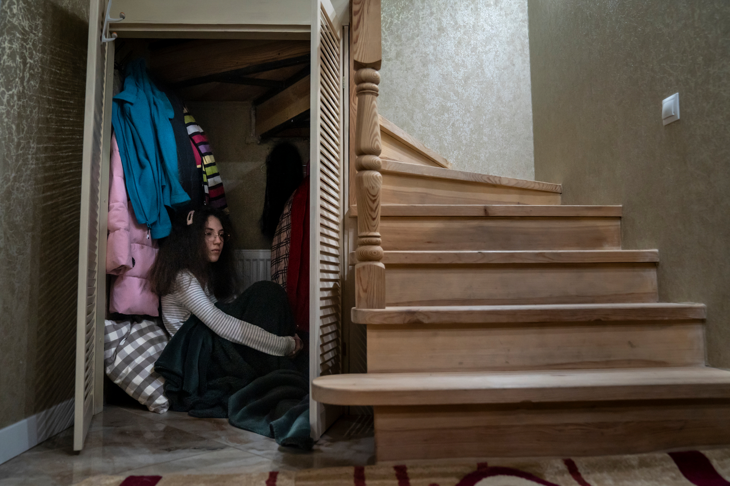 Una niña se sienta en un armario bajo la escalera de su casa.