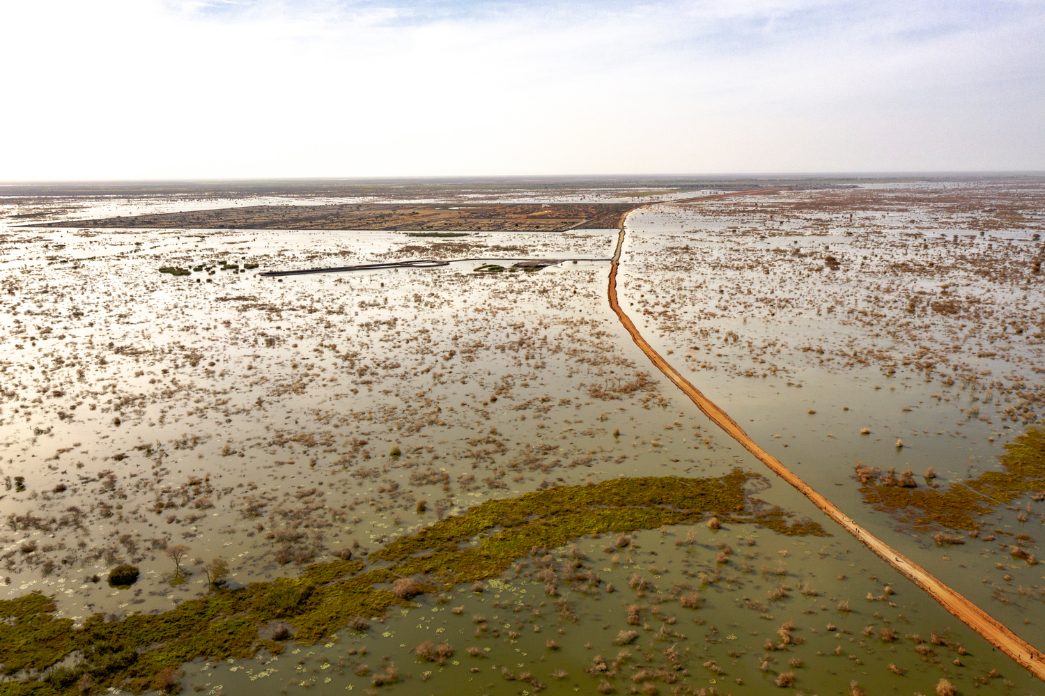 A single road, surrounded by flood waters, leads to a distant camp. Una única carretera, rodeada por el agua de la inundación, conduce a un campamento lejano.