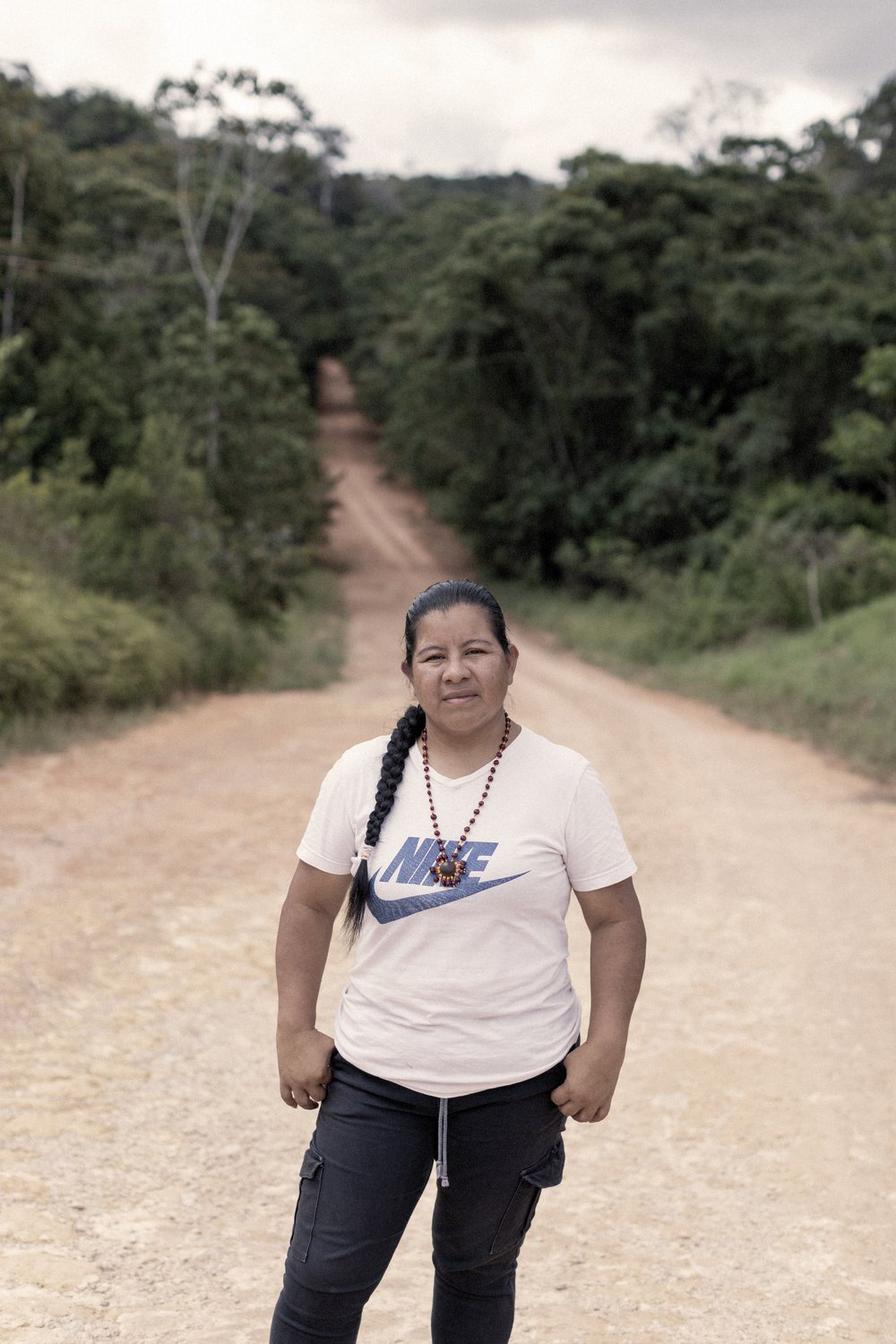 Una mujer se encuentra en un camino de tierra que atraviesa un bosque