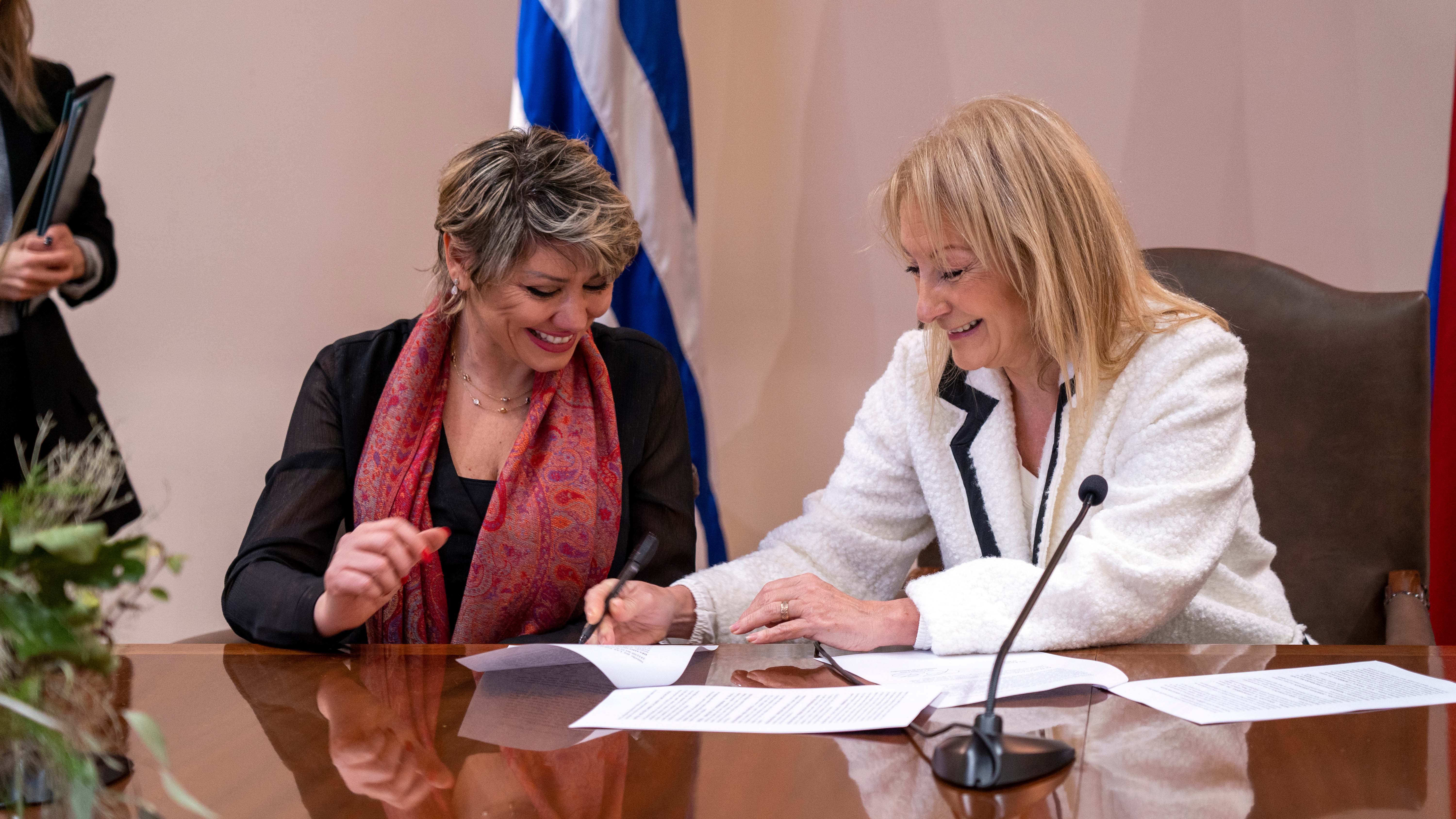 Dos mujeres con vestimenta formal firman un documento