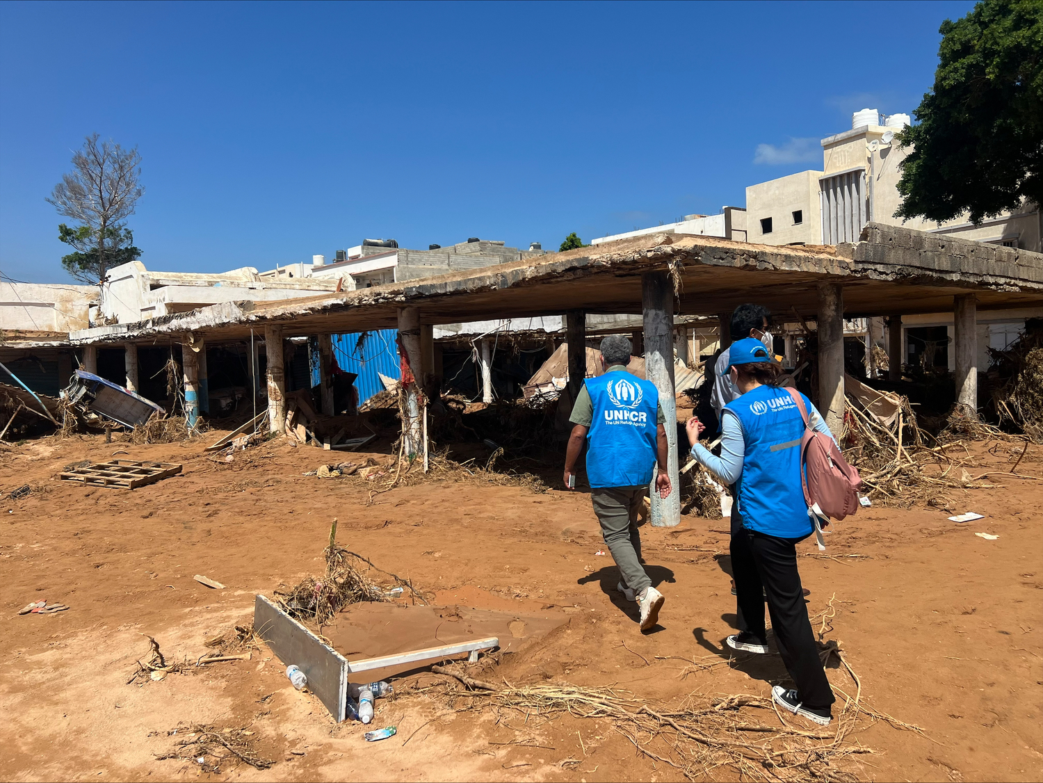 Dos trabajadores de ACNUR caminan frente a un edificio en ruinas