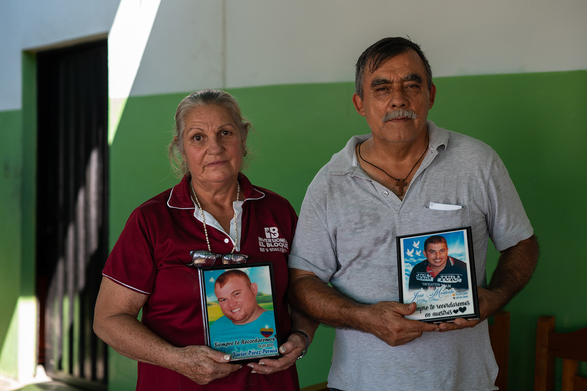 una mujer y un hombre mayores posan sujetando las fotos de dos hombres jóvenes.