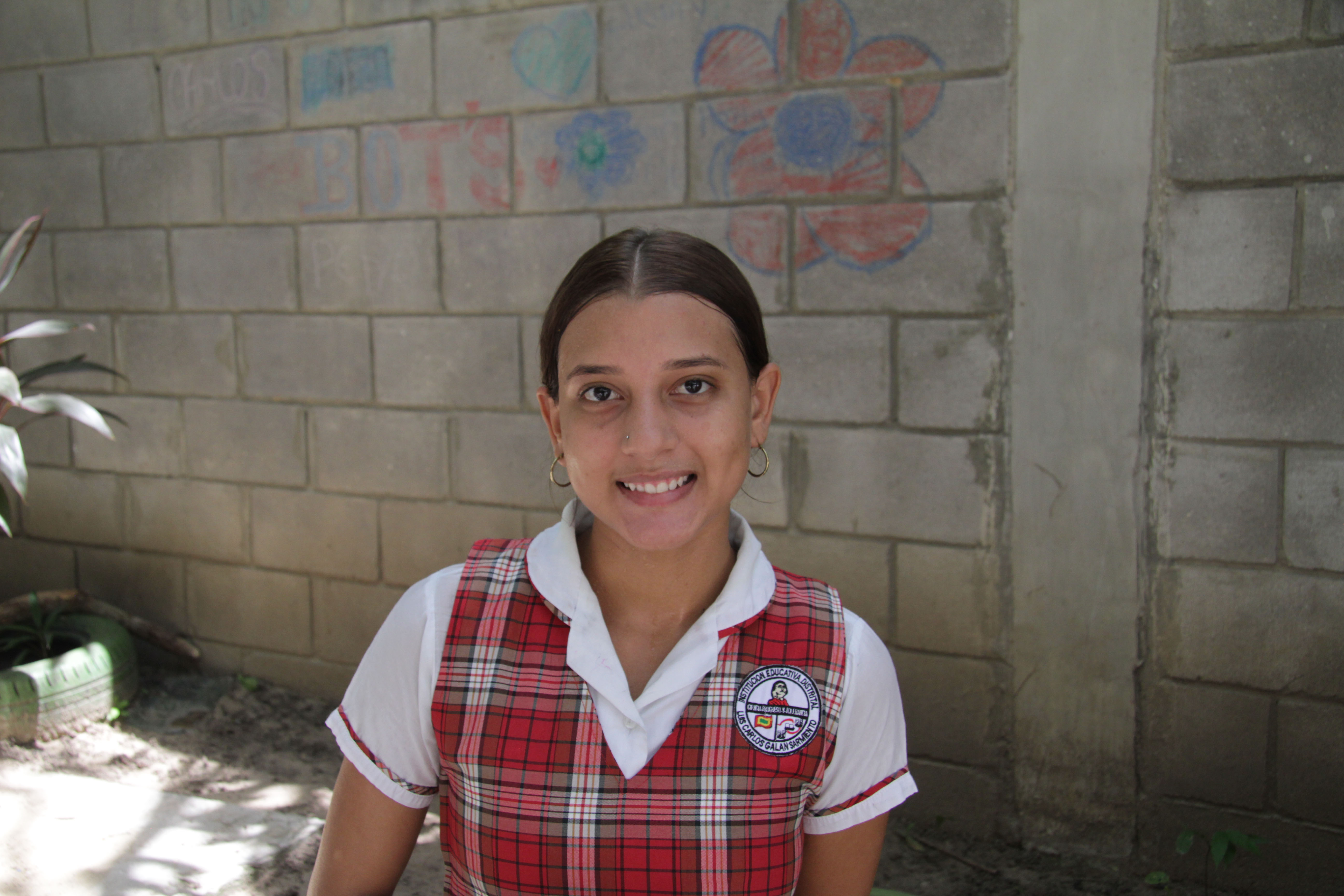 Una estudiante con uniforme rojo a cuadros, sonríe para la foto.