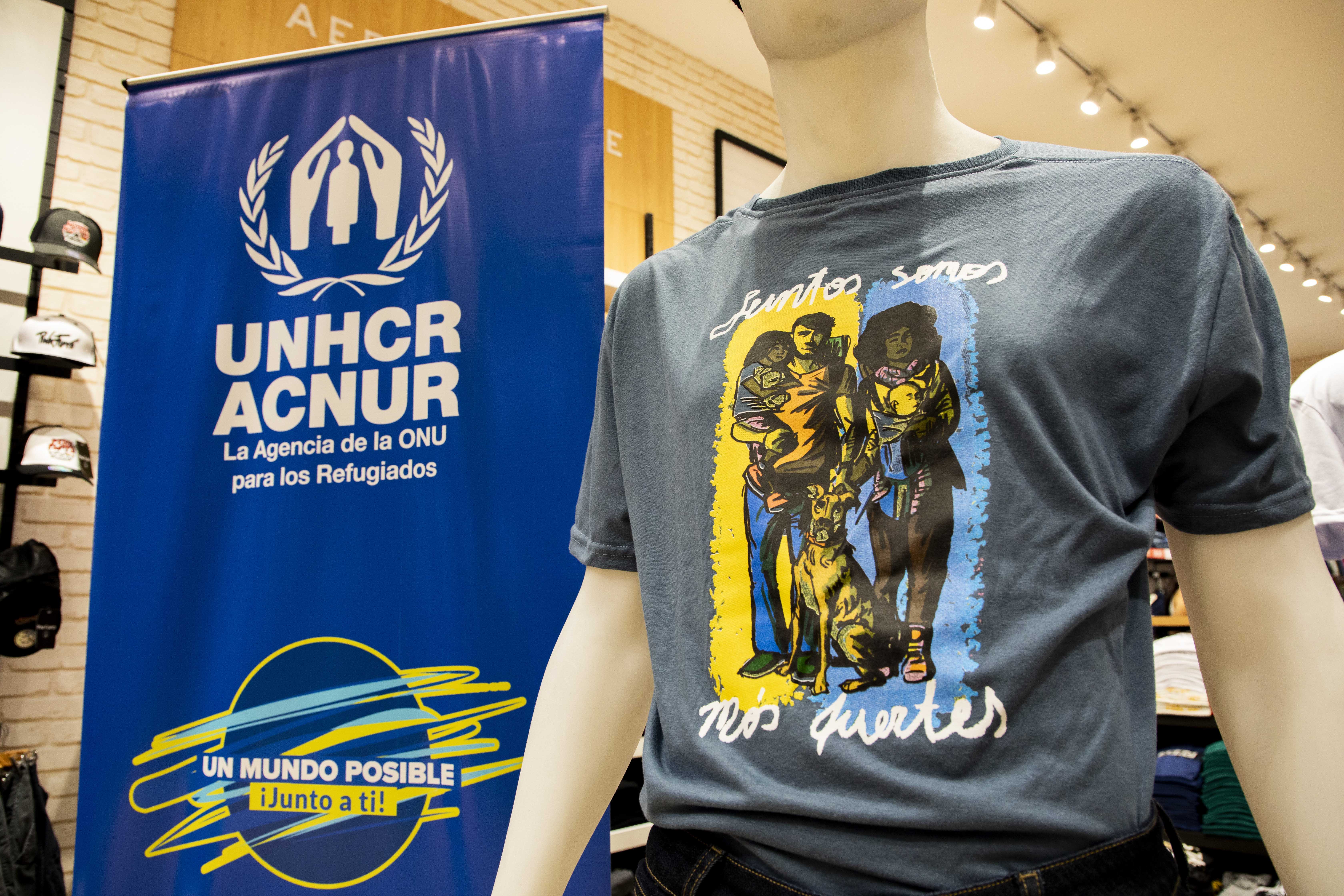 Un banner con el logo de ACNUR junto a un maniquí que lleva una camiseta con una ilustración impresa