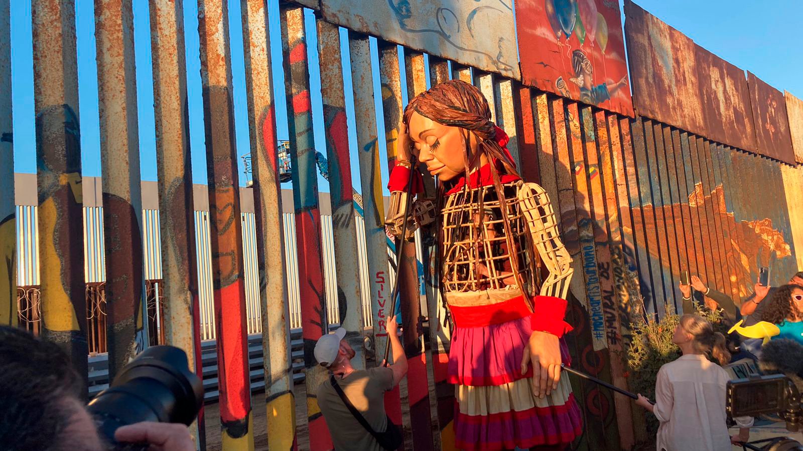 La pequeña Amal, una marioneta de 3,5 metros de altura que representa a una niña siria refugiada, recostada contra el muro fronterizo que separa Estados Unidos de México, en Tijuana. La pequeña Amal, una marioneta de 3,5 metros de altura que representa a una niña siria refugiada, recostada contra el muro fronterizo que separa Estados Unidos de México, en Tijuana.