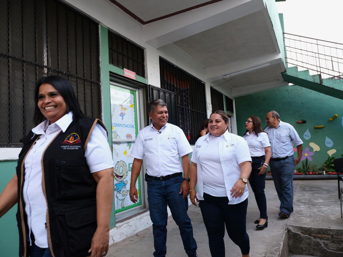 Dos hombres y tres mujeres que visten uniforme de docente, están parados afuera de aulas de clases
