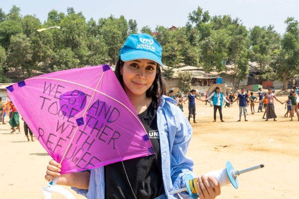 Una mujer que lleva puesta una gorra azul con el logotipo de ACNUR sonríe a la cámara mientras sostiene una cometa