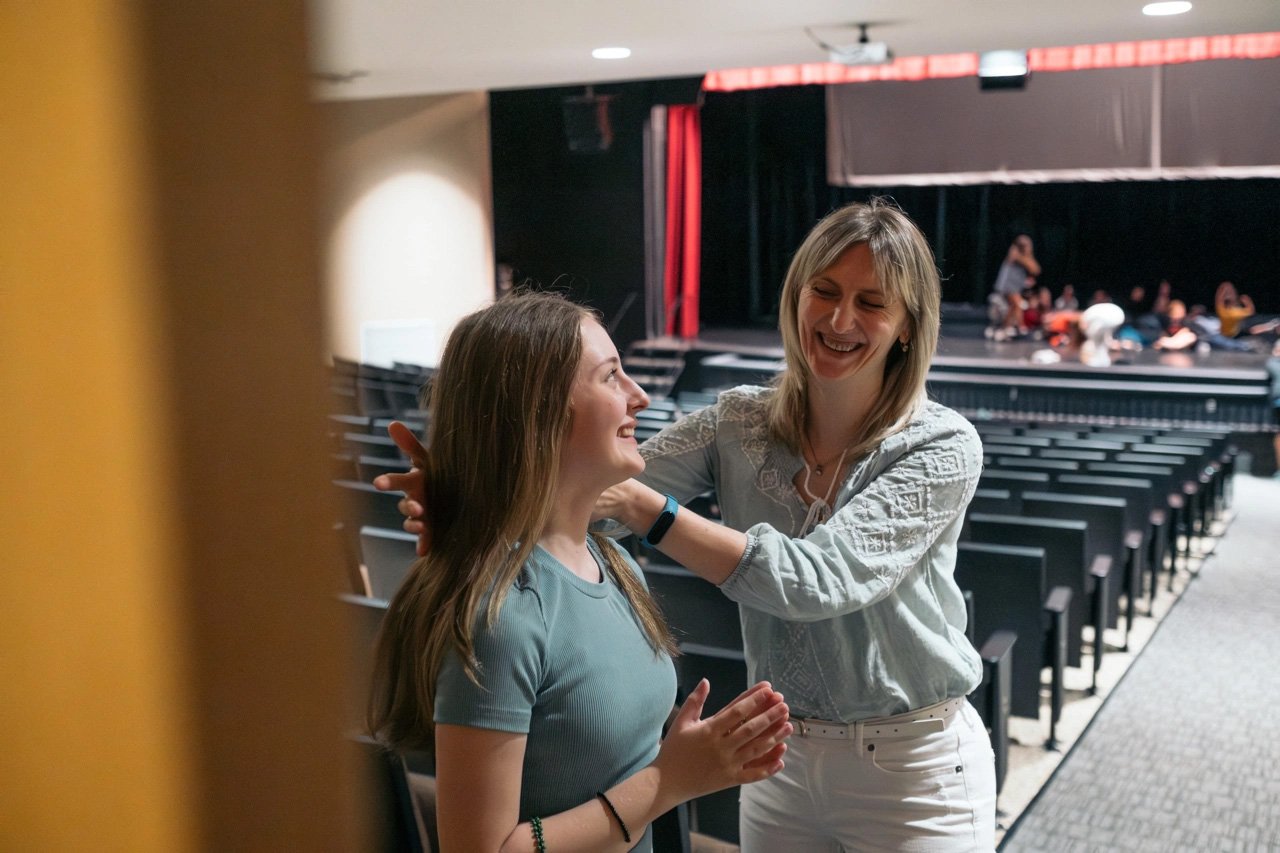 En un auditorio, una mujer le acomoda el cabello a una adolescente