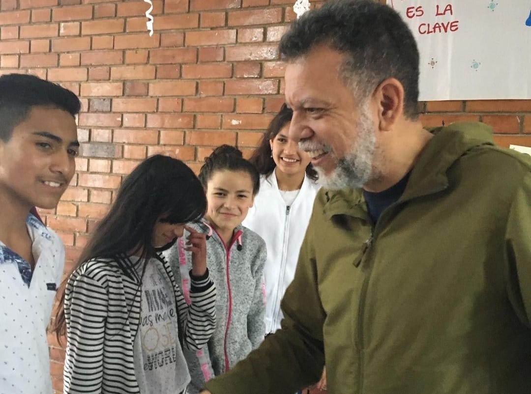 Un hombre de cabello negro y barba canosa charla con un joven