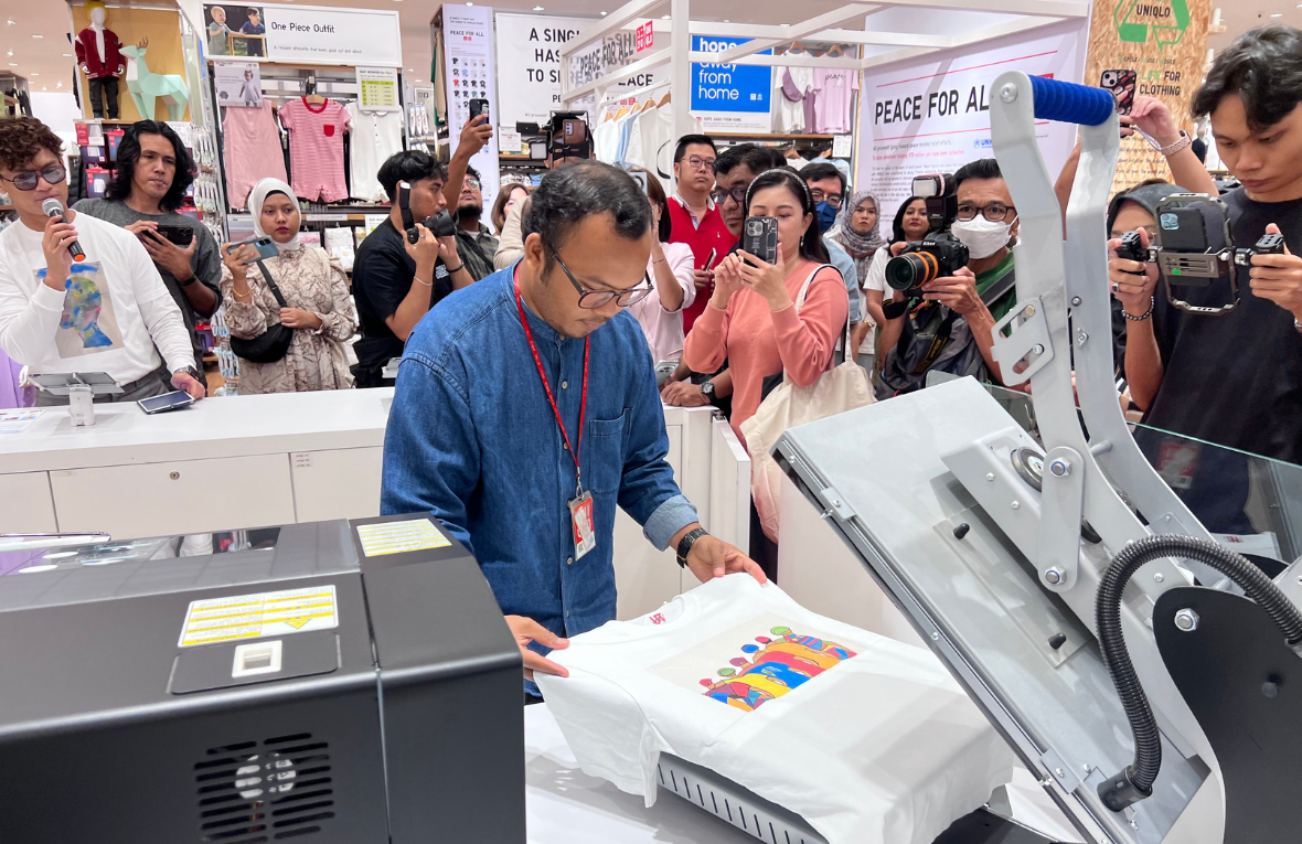 Un hombre le muestra a una grupo de personas cómo se imprimen las ilustraciones ganadoras en las camisetas que luego se ponen a la venta