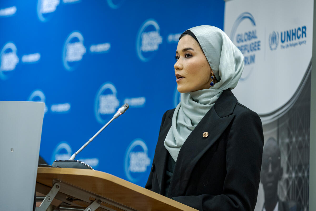 Una mujer afgana que lleva puesto el hijab emite un discurso desde un podio. Detrás suyo, un fondo azul con el logotipo de ACNUR.