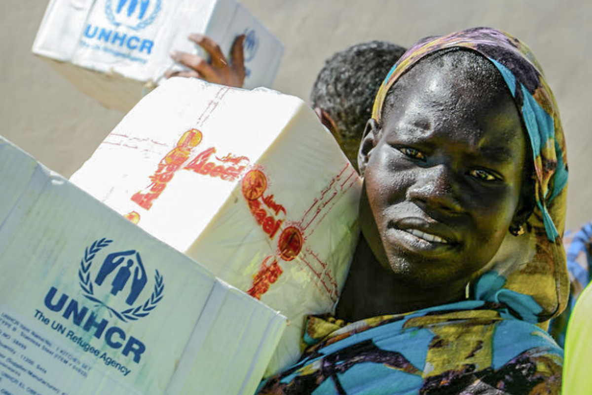 A refugee carries a box of supplies from UNHCR.