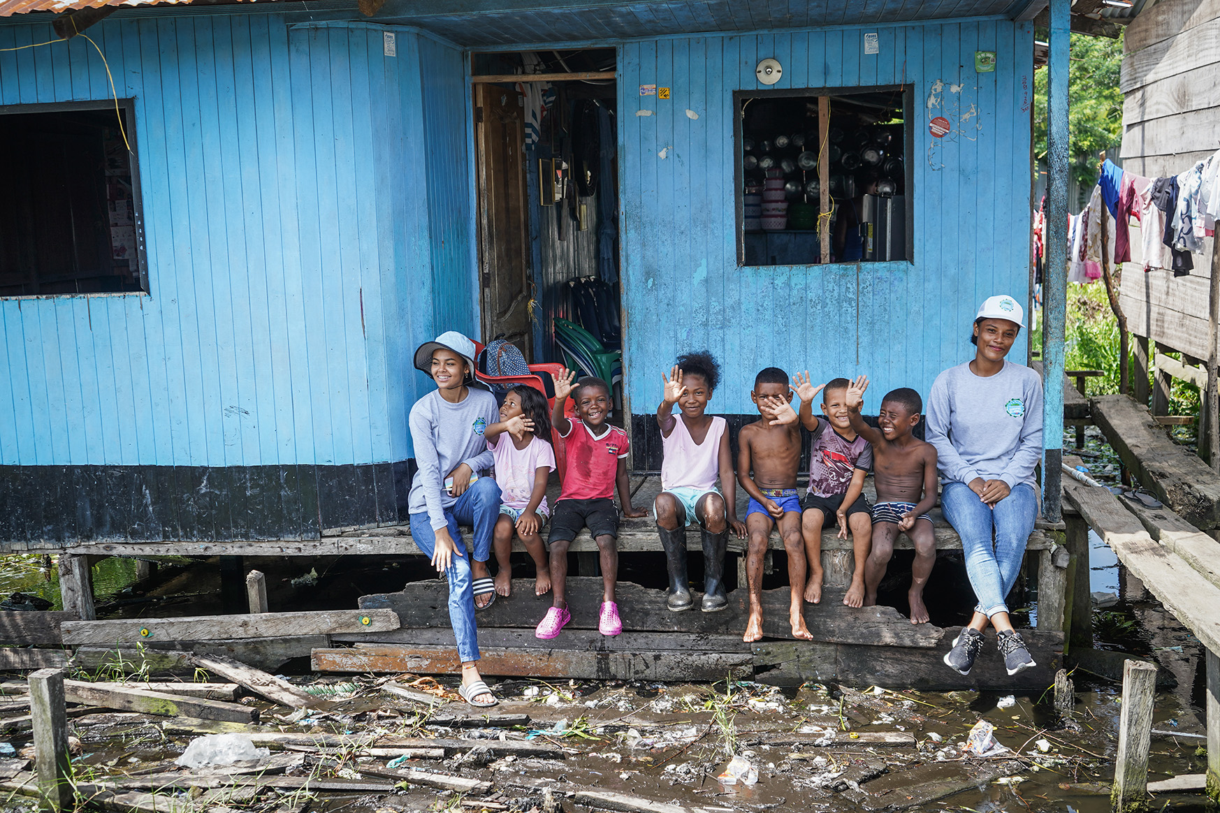 Un grupo de mujeres, niñas y niños sentados en un banco delante de una casa.