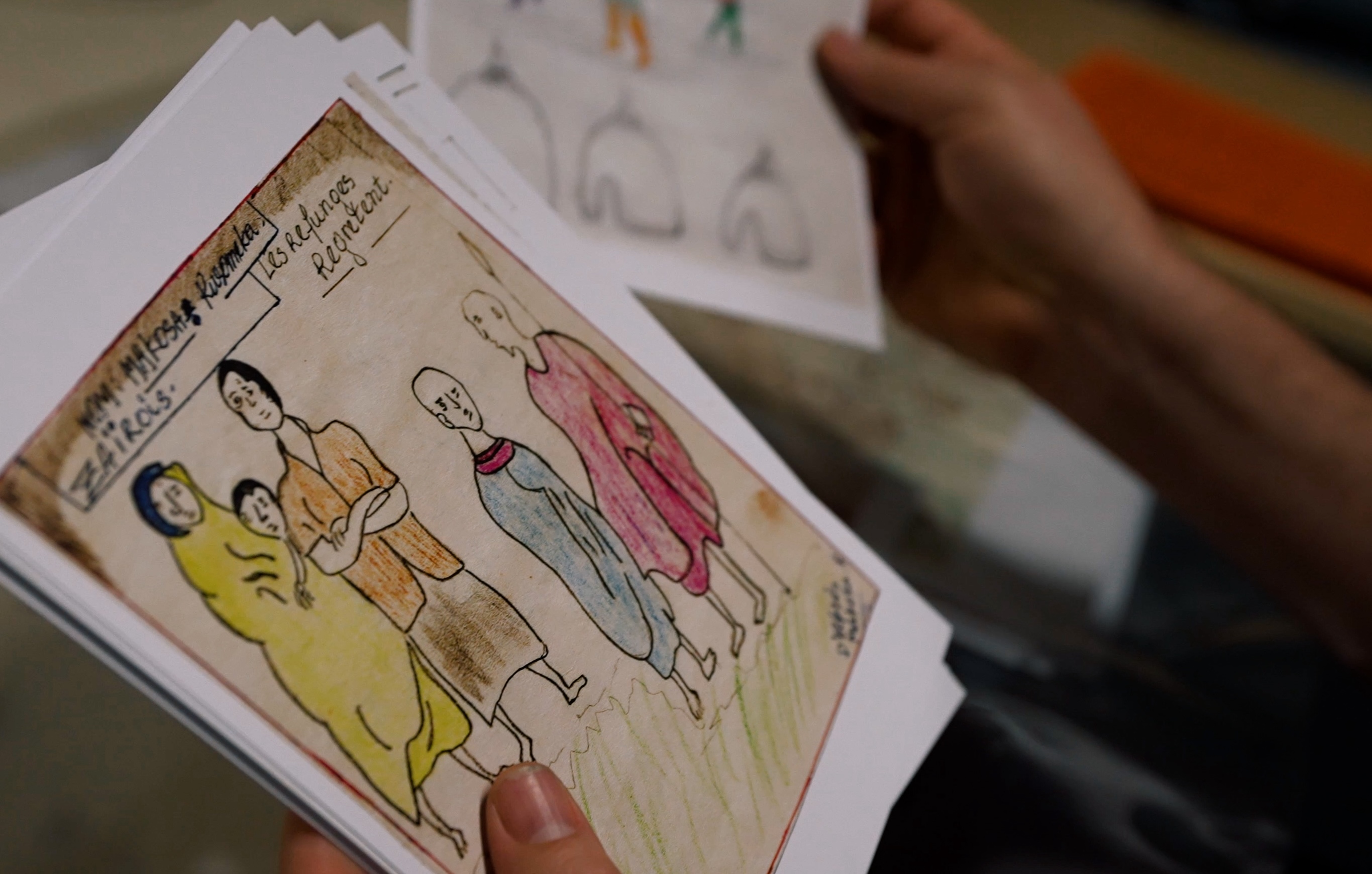 Primer plano de la manos de una persona sosteniendo dibujos infantiles de figuras de colores