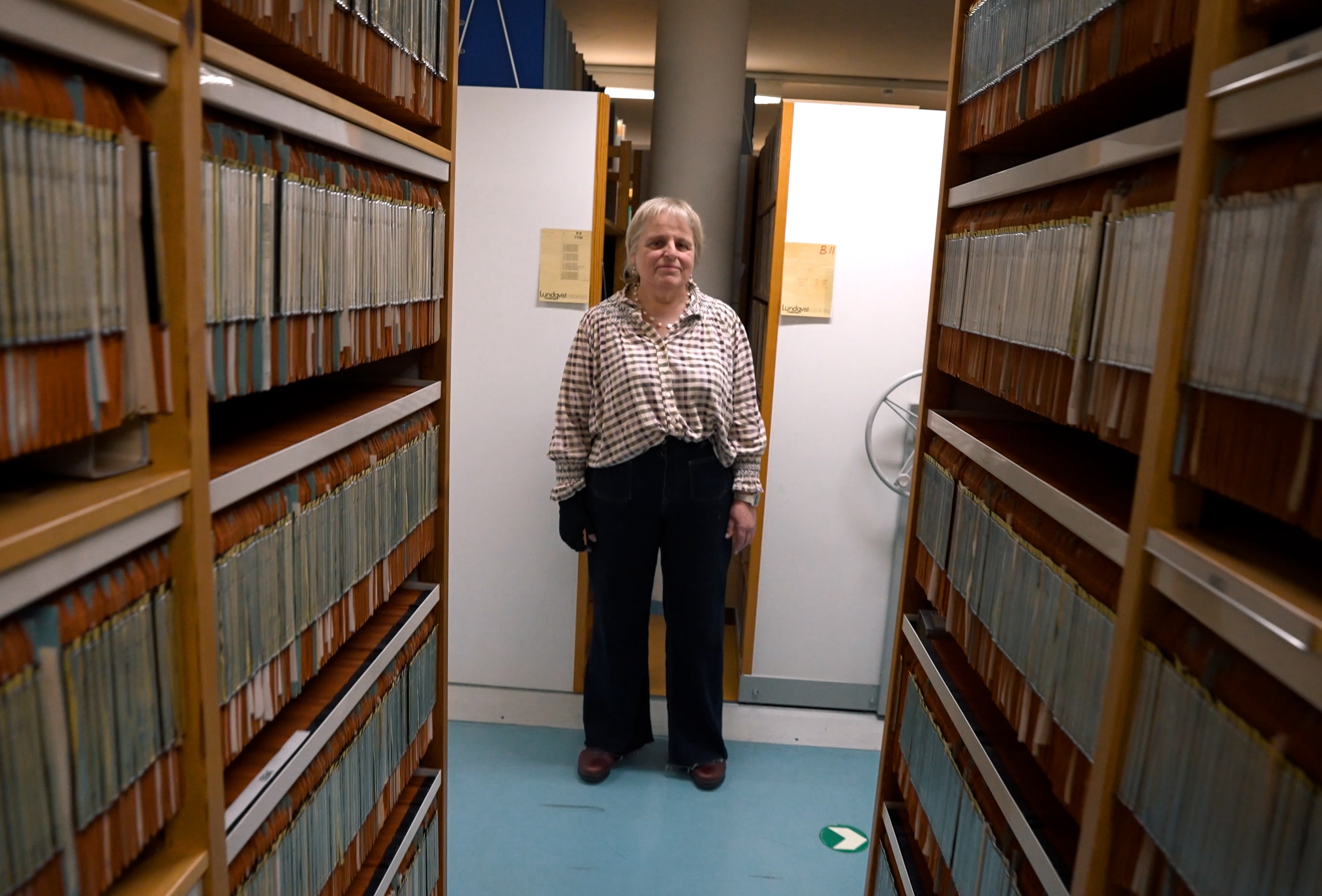 Una mujer al final de una fila de estanterías de archivos.
