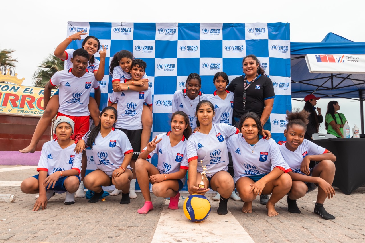 Un grupo de niñas y niños posa como lo haría un equipo de fútbol; detrás suyo, una lona con el logotipo de ACNUR