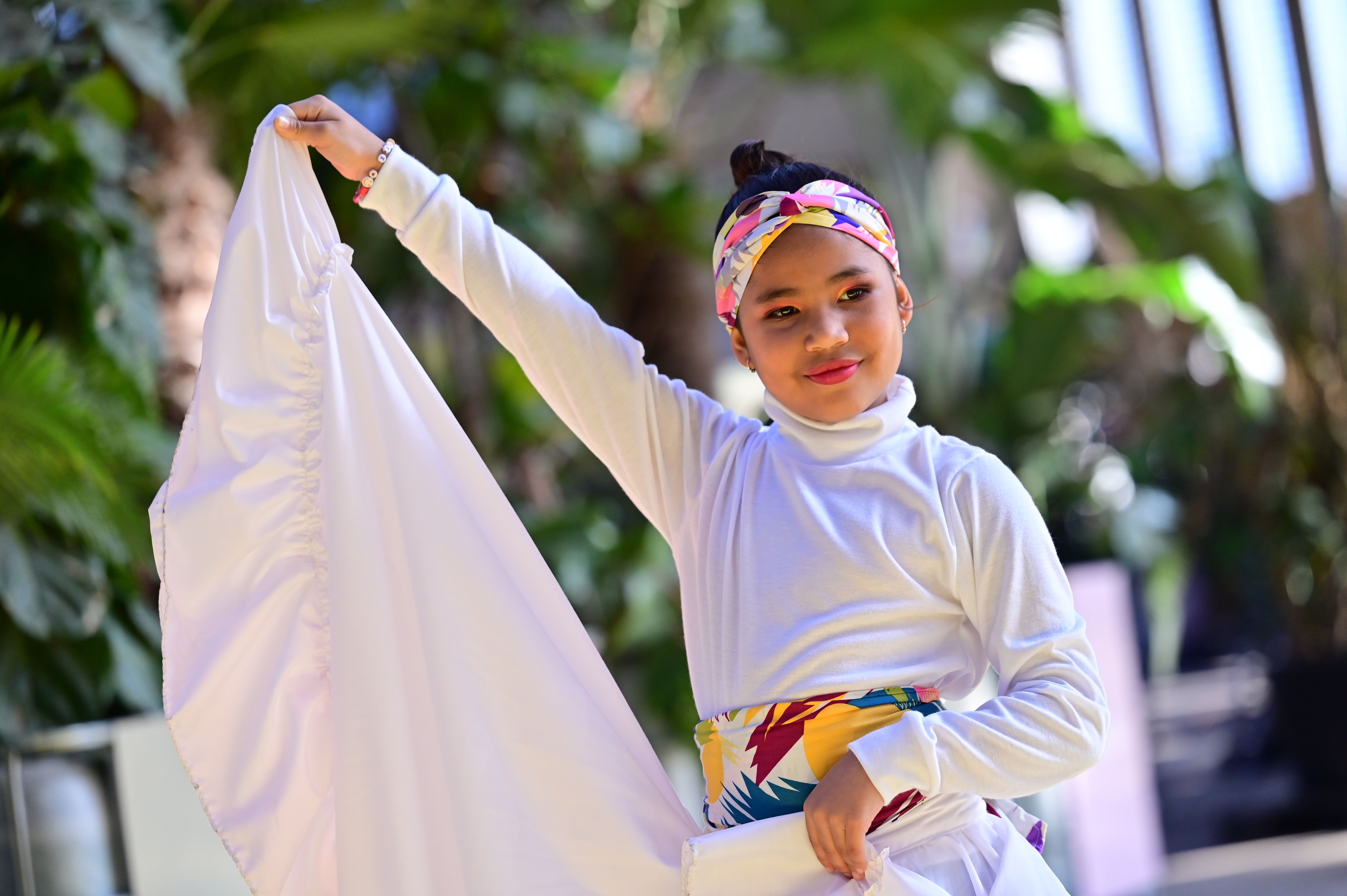 Una niña bailando: lleva puesto un vestido blanco con una banda colorida en la cintura.