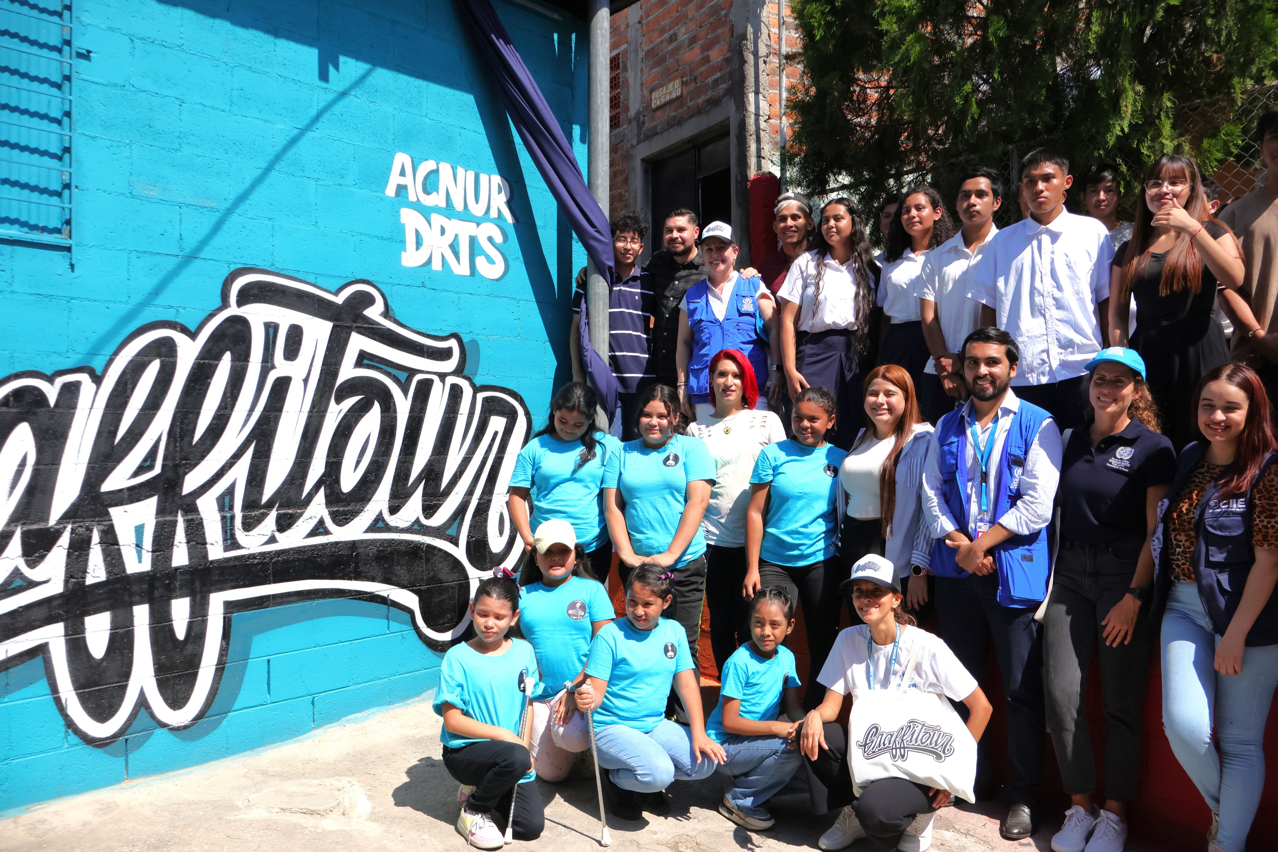 Jóvenes posan por una foto de grupo al lado de un mural.