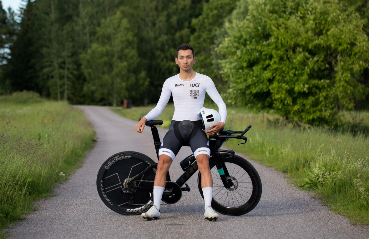 Un hombre con ropa deportiva posa junto a su bicicleta mientras sostiene un caso con su mano izquierda