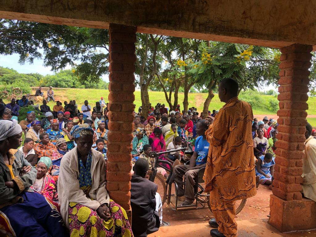 Un grupo de personas con discapacidad refugiadas en Malawi escuchan a un orador al aire libre