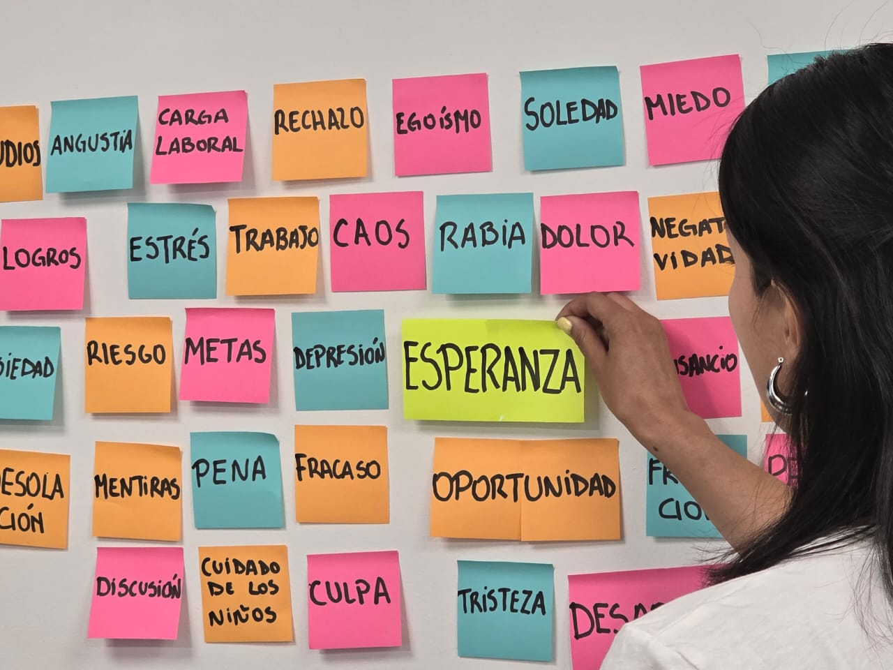 Una mujer completa la palabra “esperanza” con dos trozos de papel color amarillo en una pared llena de papeles para notas de colores donde pueden leerse palabras relacionadas con la terapia psicológica