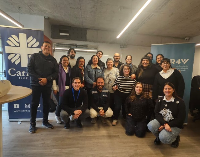Un grupo de dieciocho personas en un salón de conferencias con dos letreros azules detrás