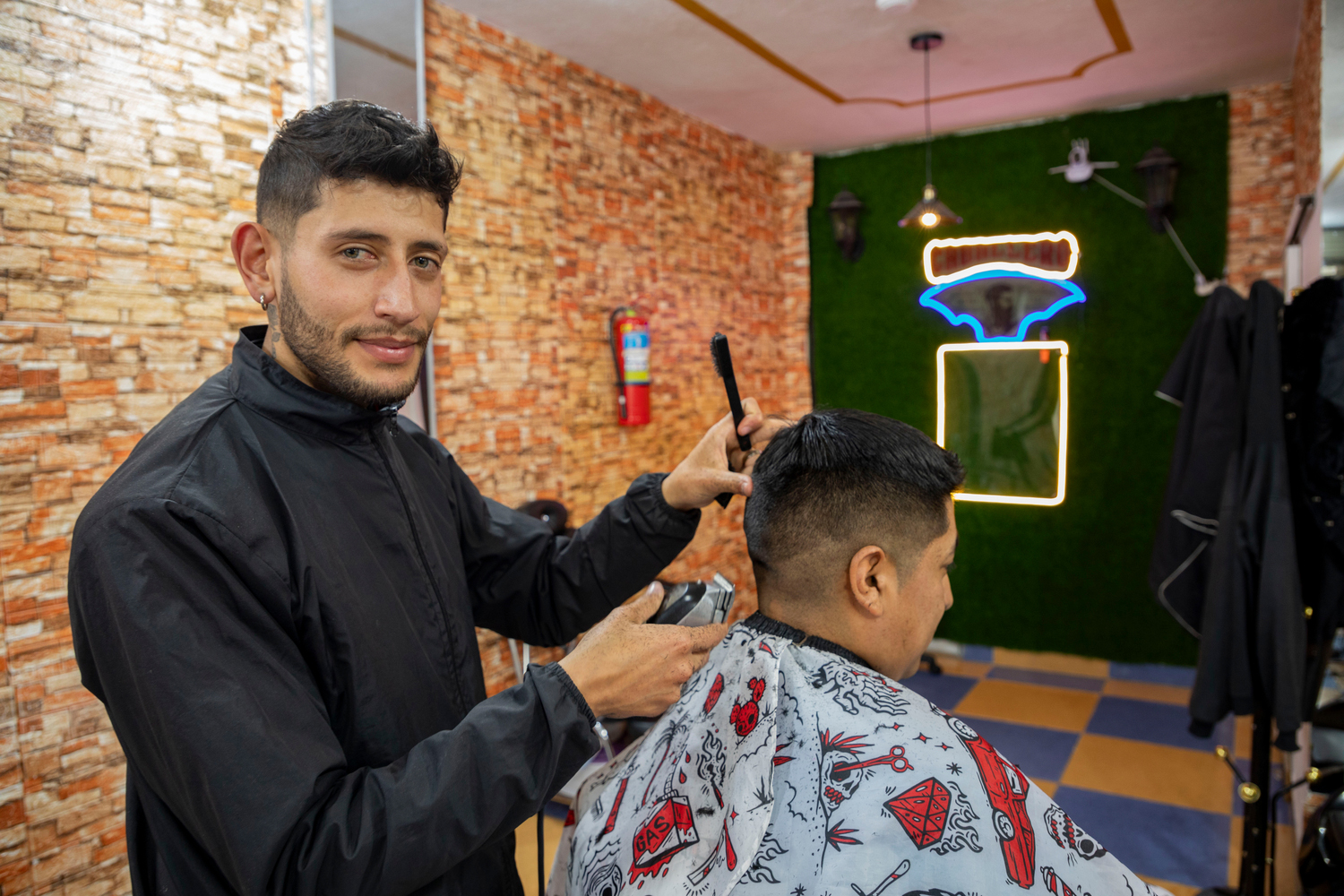 Un barbero posa para la cámara mietras le hace un corte a un cliente.