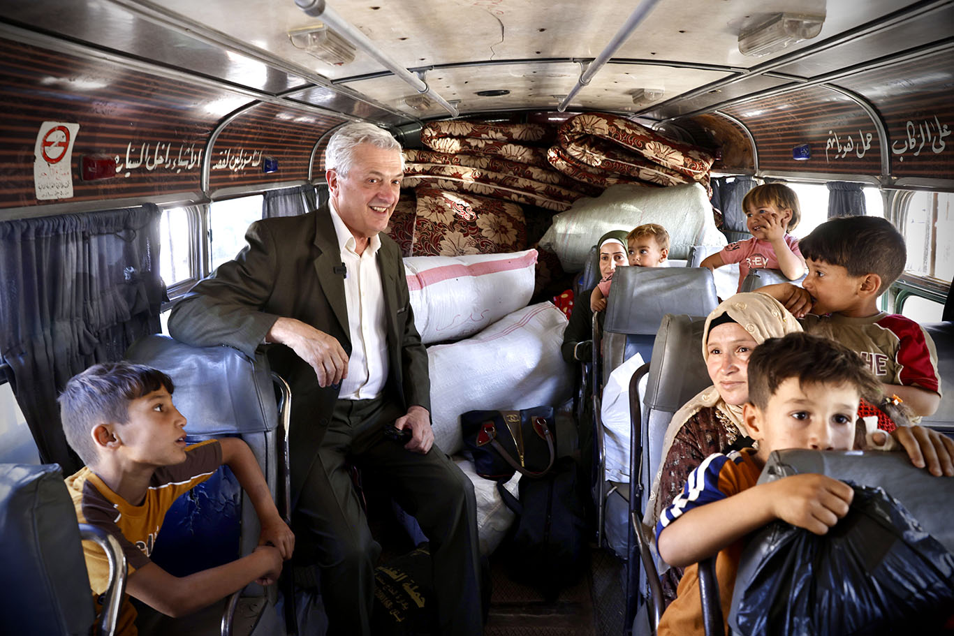 En esta foto tomada dentro de un bus el Alto Comisionado posa junto a los pasajeros, mujeres niñas y niños.