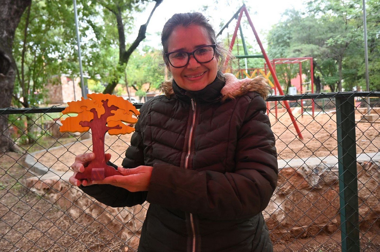 Una mujer posa frente a cámara mostrando un árbol de madera tallada.