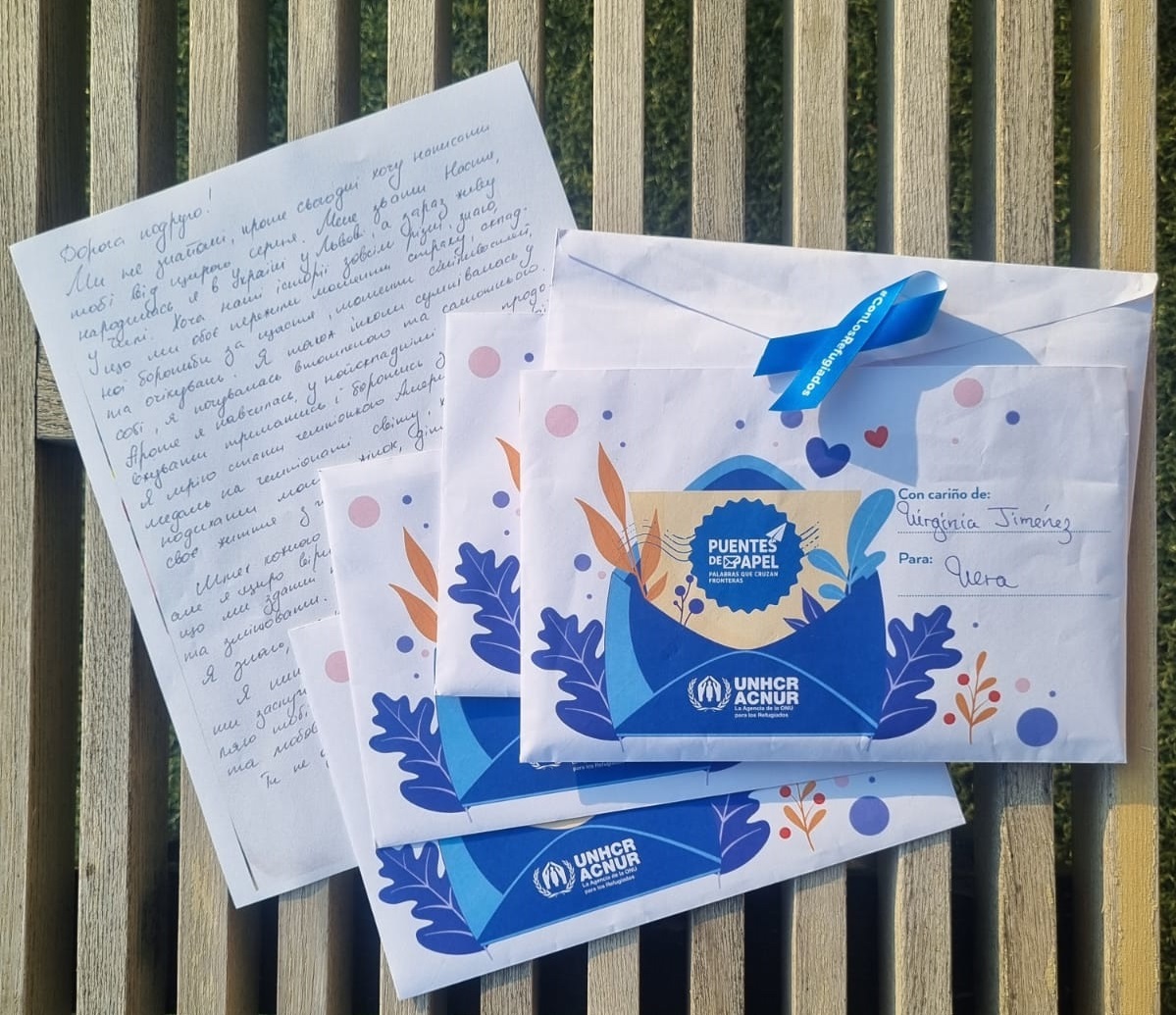 Una carta escrita a mano con tinta negra en una hoja de papel blanco, y sobre de esta, tres sobres con decoraciones azules