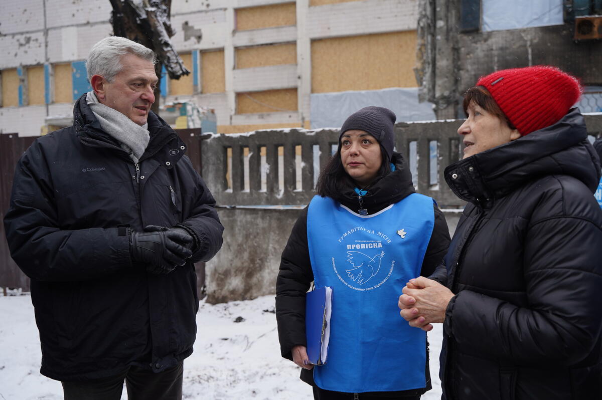 En un paisaje urbano nevado, un hombre muy abrigado charla con dos mujeres.