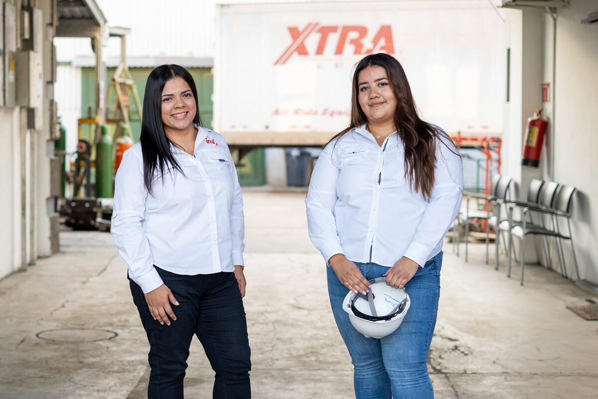 Dos mujeres de camisa blanca miran a cámara sonriendo.
