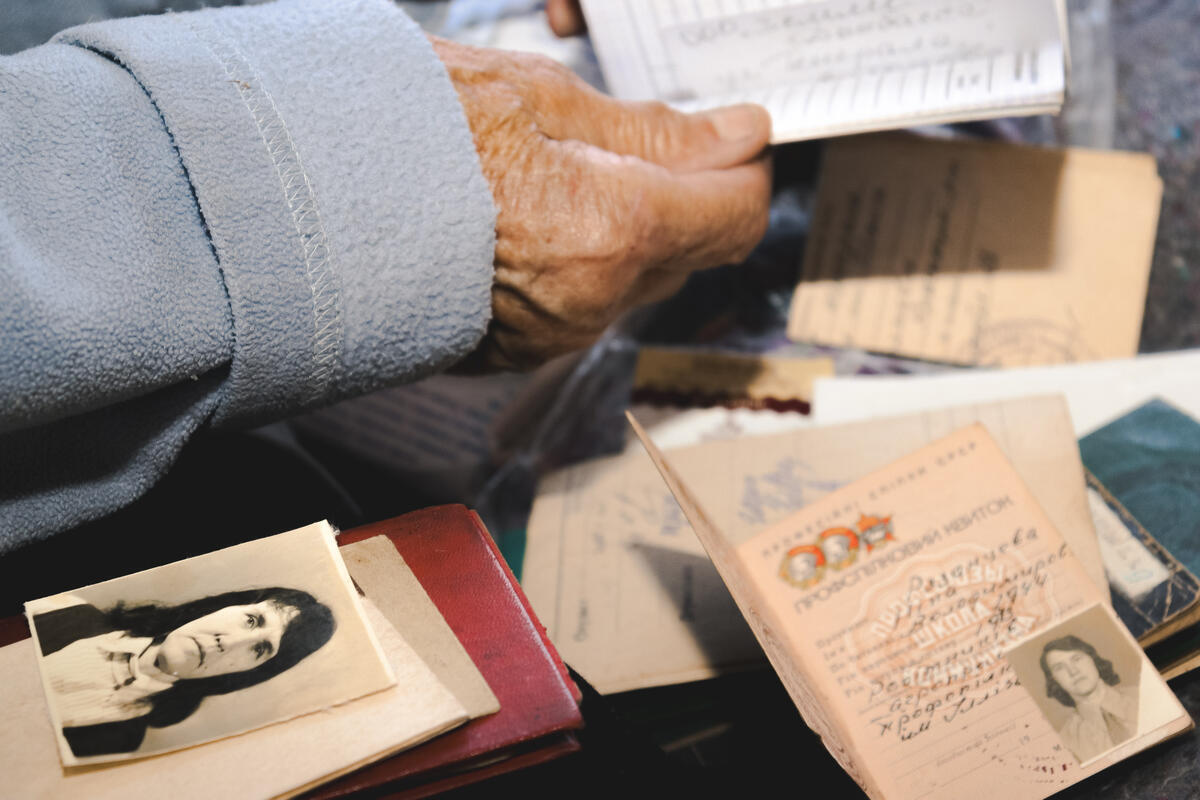 Una mano sostiene un documento mientras se extienden otros documentos y una foto antigua