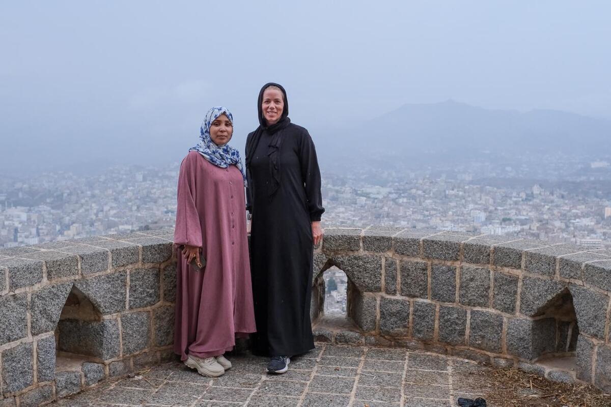 Dos mujeres posan juntas para una foto en un punto panorámico de una ciudad.