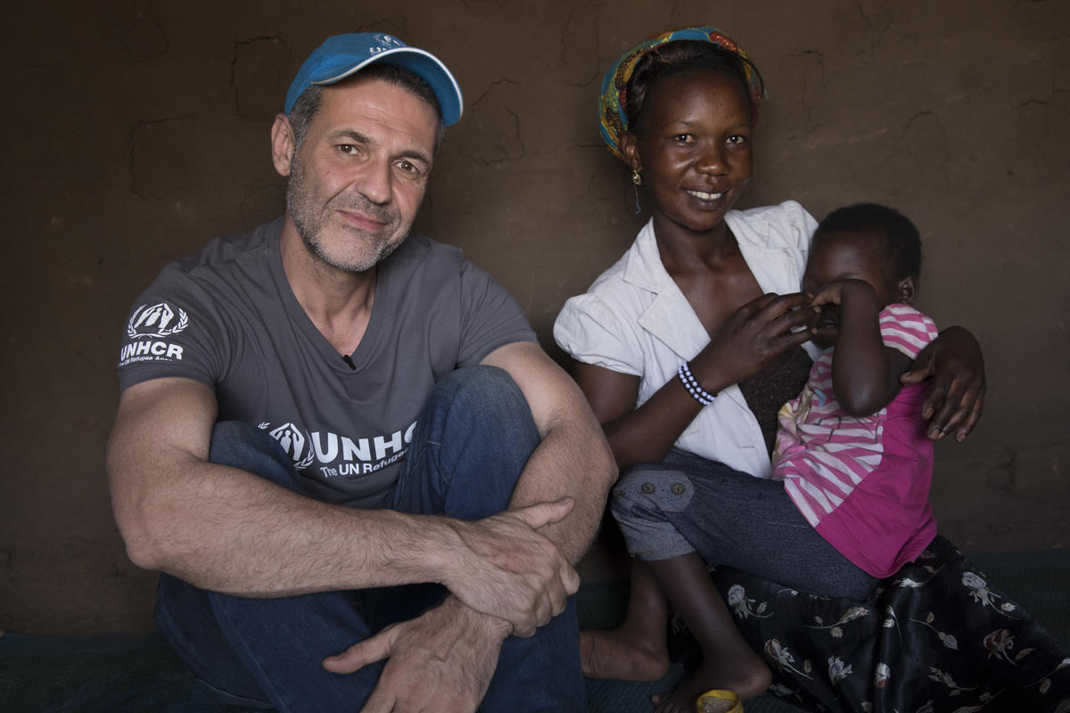 Un hombre con barba, que lleva puesta una gorra, sentado junto a una mujer africana que tiene a una cría suya en su regazo
