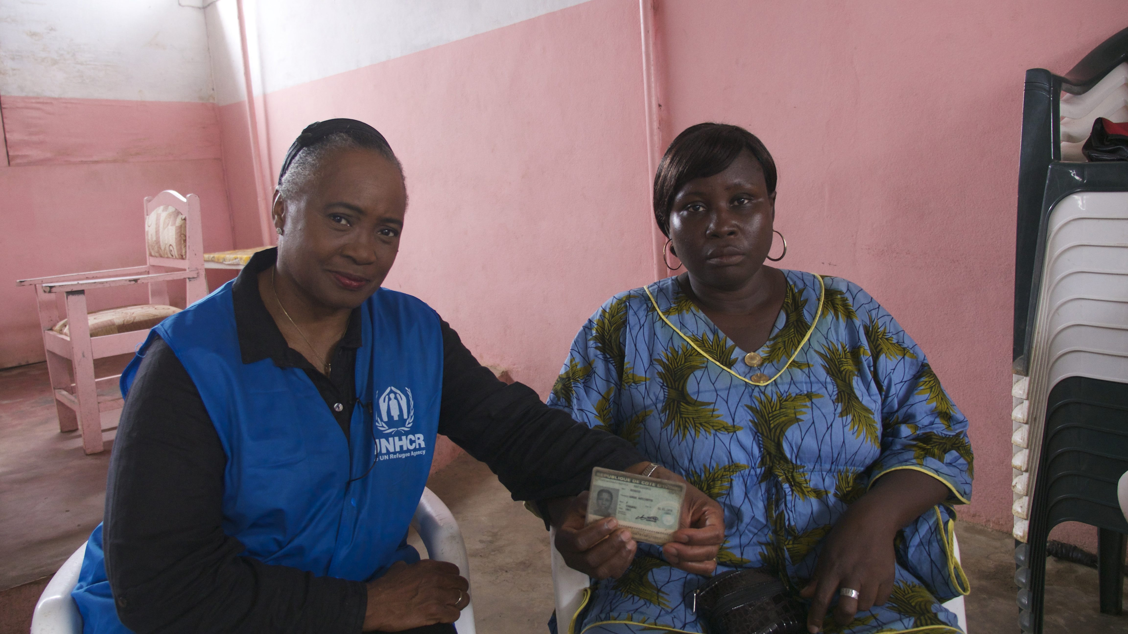 Dos mujeres afro sentadas una a lado de la otra; una de ellas muestra su documento de identidad.