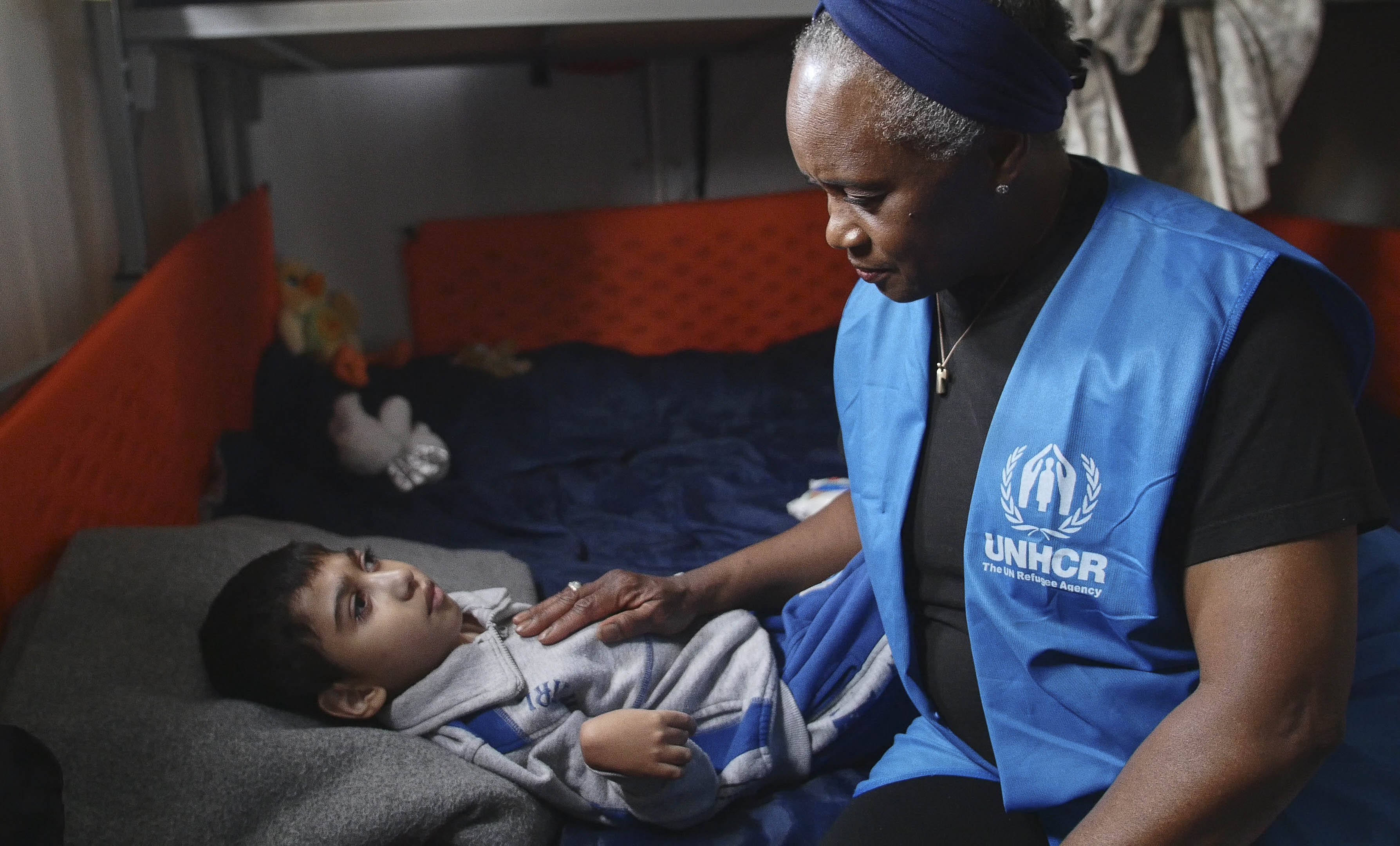 Una mujer afroestadunidense sentada junto a un niño que está postrado en una cama por la discapacidad con la que vive
