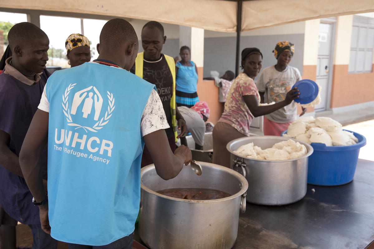 Un grupo de personas se dispone a repartir alimentos. Frente a ellas, un trabajador de ACNUR que lleva puesto un chaleco azul con el logotipo de la organización.