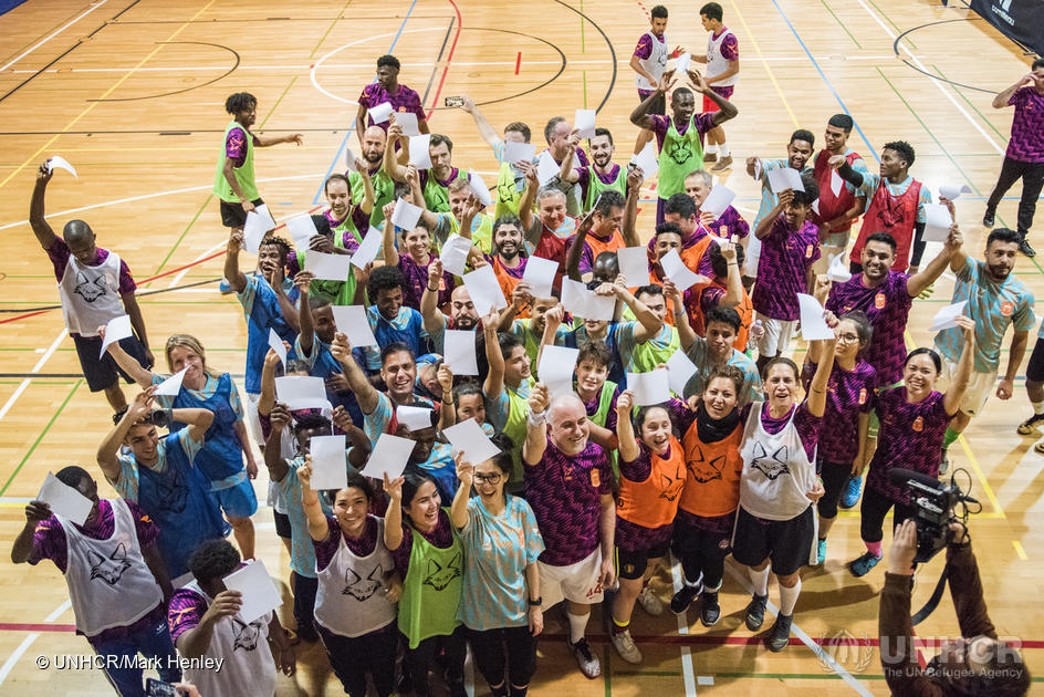 Un grupo de personas vestidas con ropa deportiva saluda a la cámara desde una cancha de baloncesto