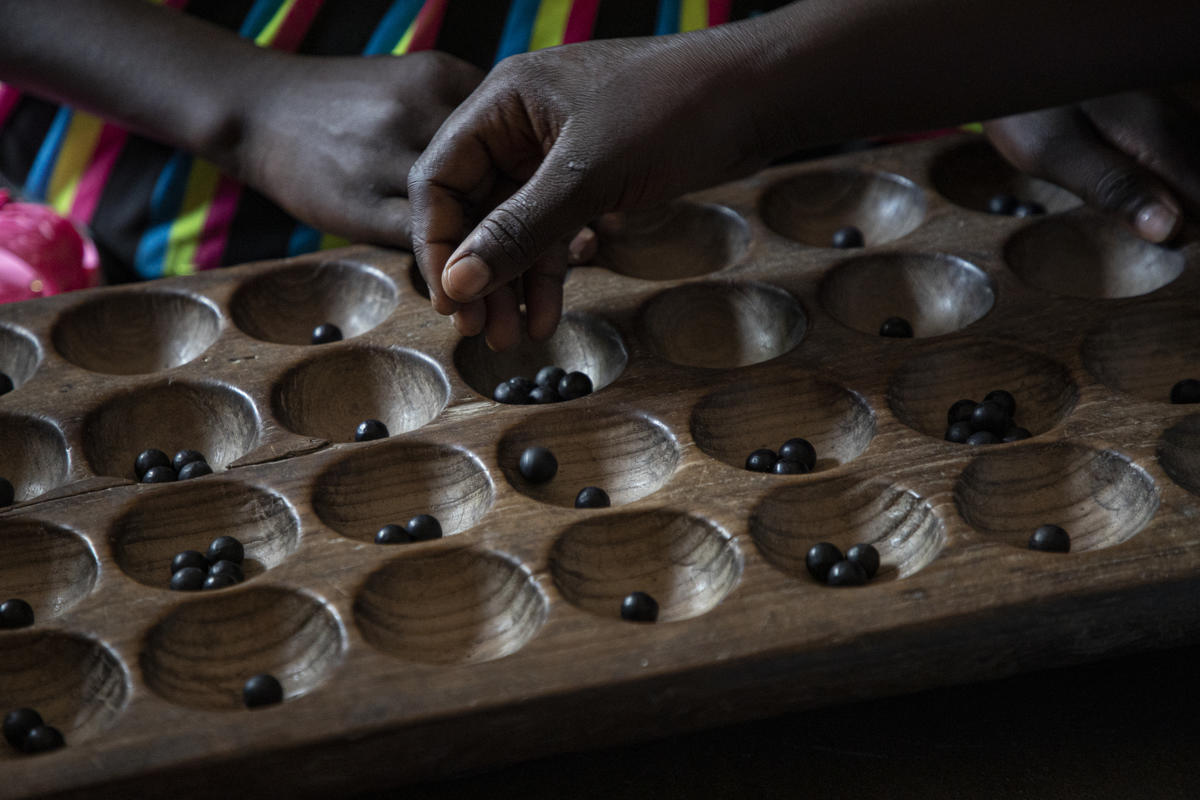 Dos manos colocando canicas en una tabla con hileras de espacios cóncavos