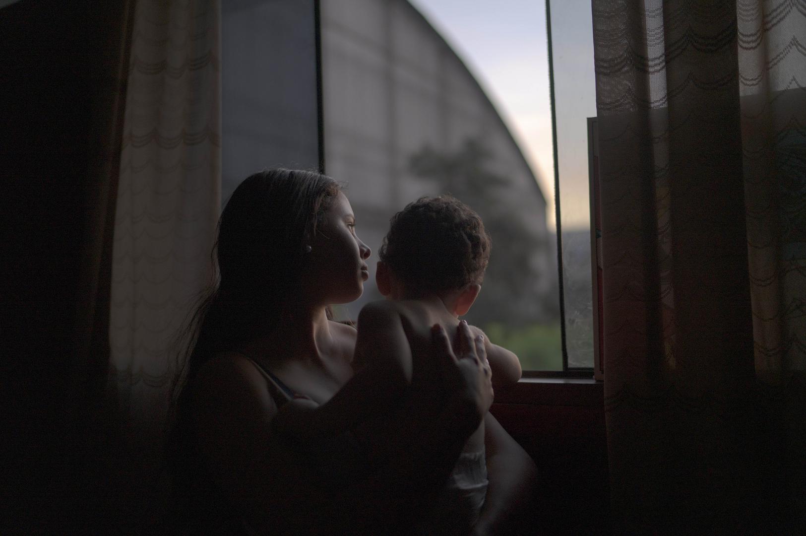 Yenifer está de pie con su hijo de 1 año junto a la ventana de la habitación en la que vive con su pareja a una hora de Lima, Perú. Llegaron a Perú en noviembre de 2019 desde Valencia, Venezuela.