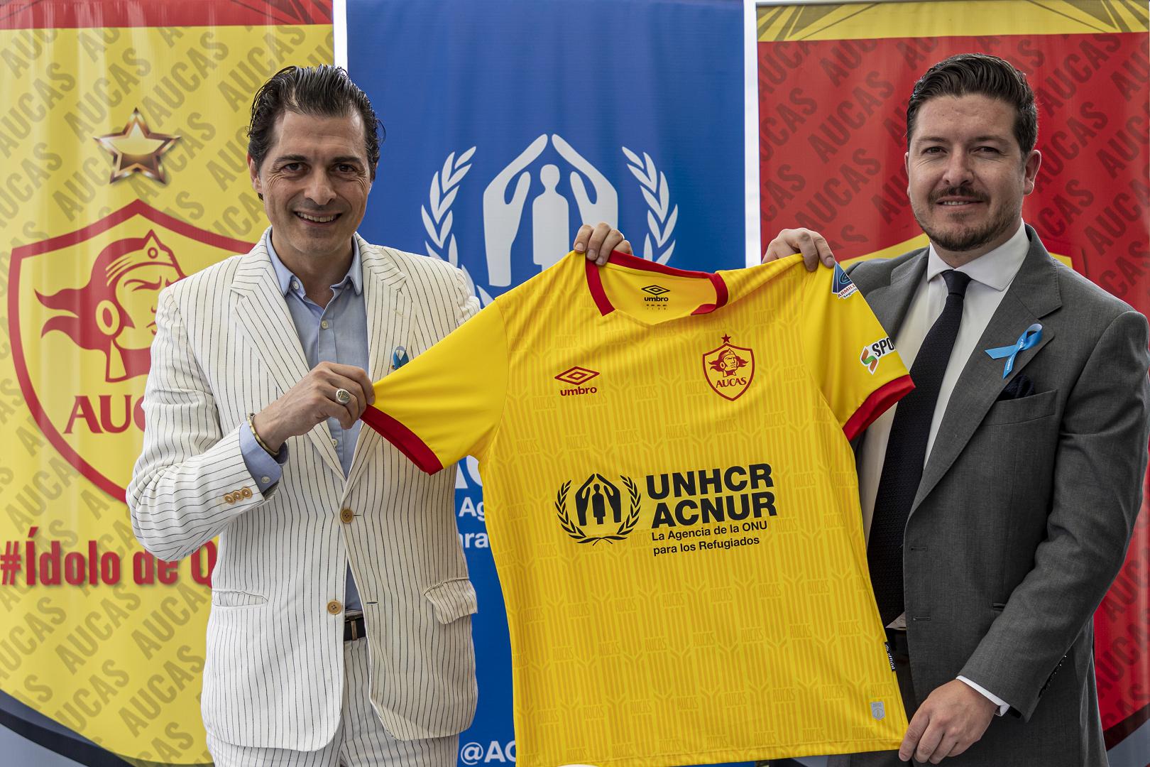 Giovanni Bassu, Representante de ACNUR en Ecuador, y Julián Pástor, Gerente General de Sociedad Deportiva Aucas, muestran la camiseta oficial del club de fútbol quiteño para el año 2023, tras la firma de un acuerdo que promoverá la inclusión de las personas refugiadas a través del deporte.
