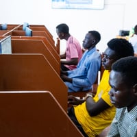 Cuatro hombres con vestimenta colorida sentados cada uno frente a una computadora en espacios divididos por módulos de madera