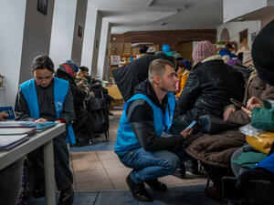 Svitlana Lokian (izquierda) y Dmytro Popsui (derecha), monitores de la protección en ACNUR, charlan con personas refugiadas de Ucrania en el edificio de Slavic Mission en Cracovia, Polonia.